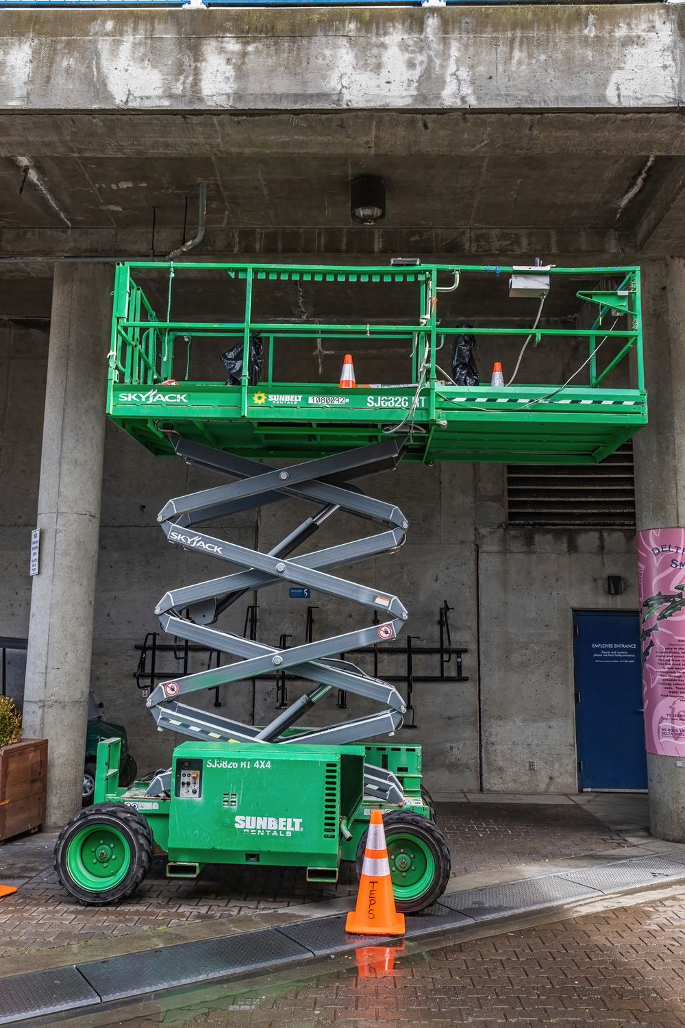 Green electric scissor lift with safety cones