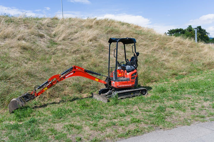 Red compact mini excavator on a grassy hillside